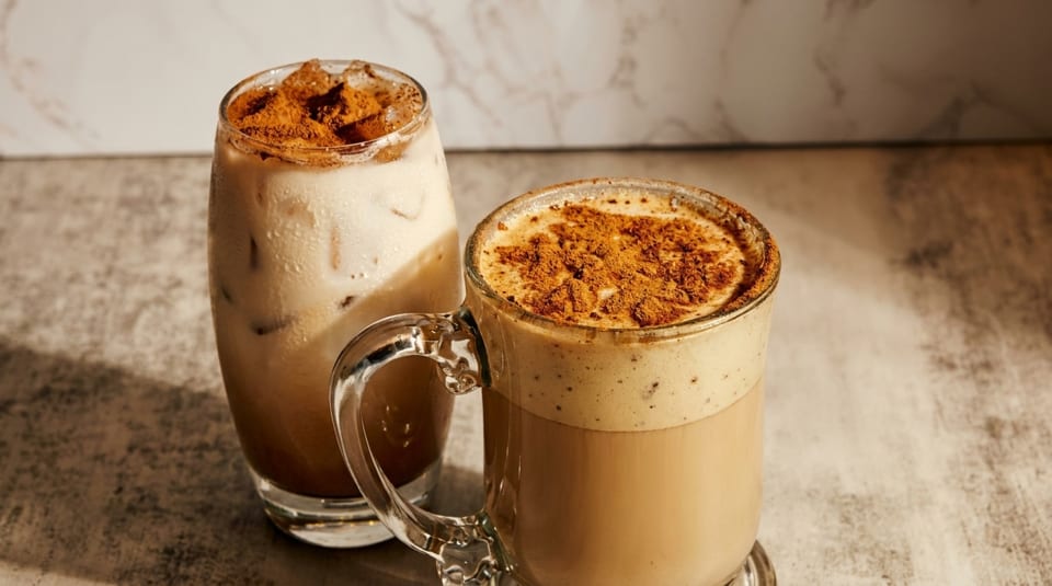 Two coffee drinks, one iced and one hot, both topped with cinnamon, on a marble surface.