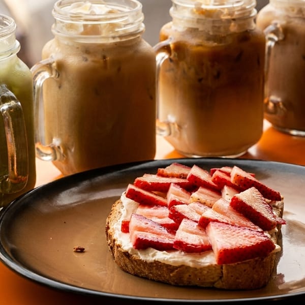 Strawberry toast with cream cheese and four iced drinks in mason jars on a wooden table.