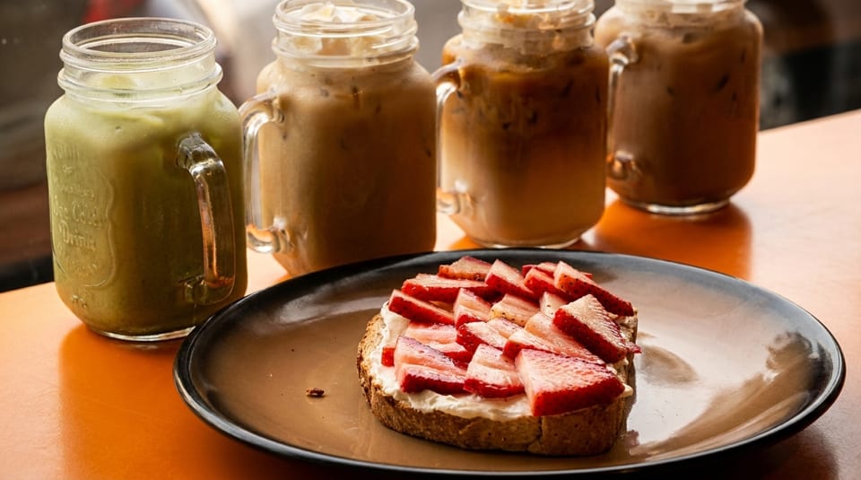 Strawberry toast with cream cheese and four iced drinks in mason jars on a wooden table.